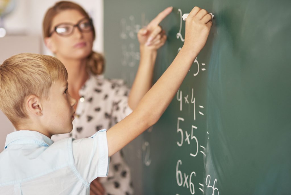 Schüler und Lehrerin vor Schultafel