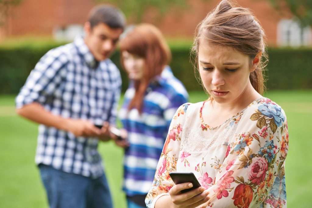 Mädchen mit Handy, im Hintergrund zwei Jugendliche